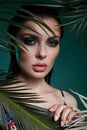 Tropical portrait sexy woman in leaves palm tree. Bright green makeup, shadow of palm leaves on girl face. Beautiful makeup