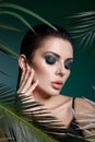 Tropical portrait sexy woman in leaves palm tree. Bright green makeup, shadow of palm leaves on girl face. Beautiful makeup