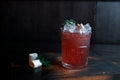 Tropical red alcoholic cocktail with the addition of: fresh juice, fruit syrup, mint, ice, fruit slices on a vintage wooden table