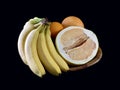 Tropical, ripe fruits in a bowl, on a black background. Yellow citrus fruits and bananas on a plate. Healthy diet: pamelo,