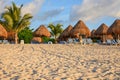 Tropical sandy beach with palms, straw umbrellas and stripy lounge chairs. Royalty Free Stock Photo