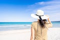 Tropical sea travel ADV banner style: unrecognizable woman holding white large hat with a hand looking to the blue ocean water Royalty Free Stock Photo