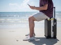 Tropical sea, Young man sitting on Travel suitcase and using smart phone at the beach. Summer holiday traveling concept design Royalty Free Stock Photo