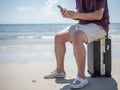 Tropical sea, Young man sitting on traveling bag and using smart phone at the beach. Summer holiday traveling concept design Royalty Free Stock Photo