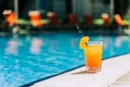 Tropical sparkling cocktail by the pool. The shot of glass with orange lemonade fruit cocktail standing near the Royalty Free Stock Photo