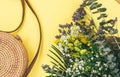 Tropical straw bag, summer flowers in bouquet on yellow background. Fashion accessories. Flat lay, close up. Summer, vacation,