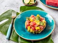 Tropical style gourmet tuna mango salad tartar with cilantro and purple onion. On blue plate, tropical leaves Royalty Free Stock Photo