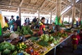 Tropical vegetables and fruits at market hall in Rabaul, Papua New Guinea. Young saleswoman wears shirt in national colors.