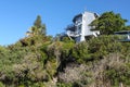 Tropical vegetation covers a hillside and almost hides steps up to a three story beach house on the top of the hill