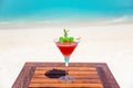 Tropical vibrant red cocktail with green sugar cherries on the wooden table at the beach and ocean Royalty Free Stock Photo