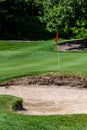 Trouble on the golf course, sand trap protecting a golf green with trees in the background, includes pin with red flag and golf ca