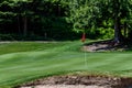 Trouble on the golf course, sand trap protecting a golf green with trees in the background, includes pin with red flag and golf ca