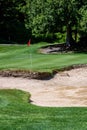 Trouble on the golf course, sand trap protecting a golf green with trees in the background, includes sand rake and pin with red fl