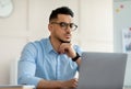 Troubled Arab office worker sitting at table, looking at laptop screen, thinking over business problem at office