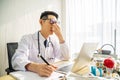 Troubled asian man doctor working on computer at desk in hospital clinic, worried, thinking hard, healthcare concept for Covid19