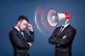 A troubled businessman stands near another man with a large shouting megaphone instead of his head. Royalty Free Stock Photo