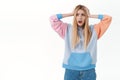 Troubled and concerned, alarmed blond girl in hoodie, hold hands on head and shaking it distressed, look away gasping
