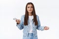 Troubled and displeased young frustrated woman in denim jacket, jeans, spread hands sideways in dismay, holding