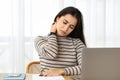 A troubled woman massages her neck while working on a laptop