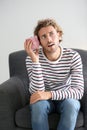 Troubled young man with piggy bank sitting in armchair at home Royalty Free Stock Photo