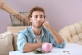Troubled young man with piggy bank at table Royalty Free Stock Photo