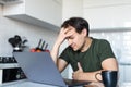 Troubled young man sit in kitchen look at laptop screen thinking pondering of problem solution, pensive male freelancer work on Royalty Free Stock Photo