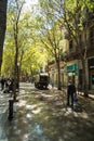 Truck of the Barcelona municipal service brigade, cleaning a pedestrian street with green trees and pedestrians walking on the wet