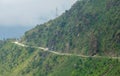 Truck and car drive down a gravel road running along the steep green mountain. Royalty Free Stock Photo