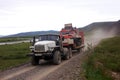 Truck carries all-terrain tracked vehicle at gravel road tundra