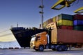 Truck carrying forty-foot container leaving port terminal with ship and quay crane on the background. Seaport operation activities