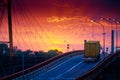 Truck with container rides over the bridge, beautiful sunset, freight cars in industrial seaport, the road goes up