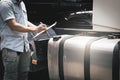 A truck driver holding clipboard safety checking a large fuel tank of semi truck