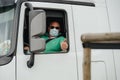 Truck driver in Mercedes-Benz Actros wearing a protection mask shows OK sign