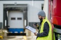 Truck driver standing by red truck and holding clipboard, looking at cargo details, delivery schedule. Royalty Free Stock Photo