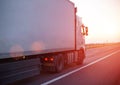 A truck with an isotherm semitrailer transports cargo along the highway against the backdrop of an evening sunset