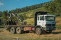 Truck log loader next to dirt road on terrain with trees