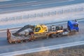 Truck with a long trailer platform for transporting heavy machinery, loaded crawler excavator with bucket. Highway transportation Royalty Free Stock Photo