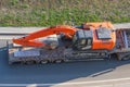 Truck with a long trailer platform for transporting heavy machinery, loaded excavator. Highway transportation Royalty Free Stock Photo