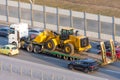 Truck with a long trailer platform for transporting heavy machinery, loaded tractor with a bucket. Highway transportation traffic Royalty Free Stock Photo