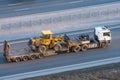 Truck with a long trailer platform for transporting heavy machinery, loaded tractor with a bucket. Highway transportation