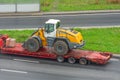 Truck with a long trailer platform for transporting heavy machinery, loaded tractor with a bucket. Highway transportation Royalty Free Stock Photo