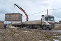 A truck with a manipulator crane unloads a construction shed