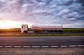 A truck with a semi-trailer tanker transports dangerous goods against the backdrop of a sunny sunset and the sky in the