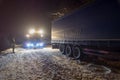 Truck traffic accident at night, on a snowy winter road. Strongly illuminated Wrecker truck pulls a truck out of snow hanging.