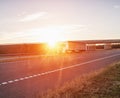 A trucker driver transports cargo on a white wagon against the background of a road bridge and a sunset. Shipping, business and