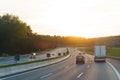 Trucks and cars drive along the highway along the forest in the rays of the setting sun.