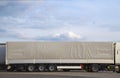 Trucks in the parking lot. In the foreground a truck with a long semi-trailer covered with a gray tarpaulin