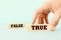 true or false concept man hand picking wooden cubes with text over wooden blue background.