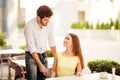 True gentleman! Young handsome brunet lover is adjusting the chair of his happy lady, both well dressed, at a sunny terrace of res Royalty Free Stock Photo