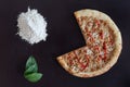 Truncated pizza, pile of flour and green leaves on black background